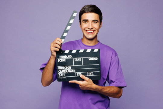 Young surprised shocked man wear violet t-shirt casual clothes hold in hand classic black film making clapperboard isolated on plain pastel light purple background studio portrait. Lifestyle concept.