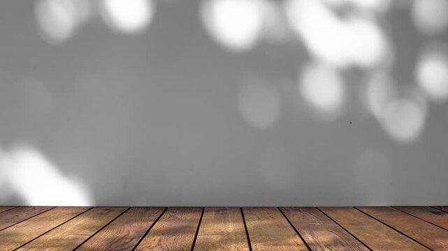 The shadow of tree leaves sways on a white background with a wooden floor