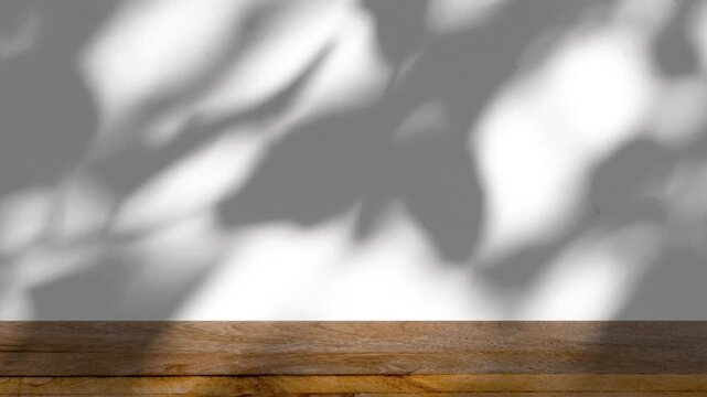 The shadow of tree leaves sways on a white background with a wooden floor