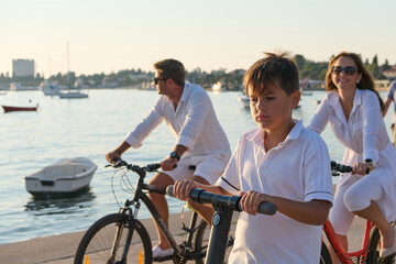 Obraz premium Family Cycling and Riding Electric Scooter Along Seaside Promenade During Sunny Summer Vacation