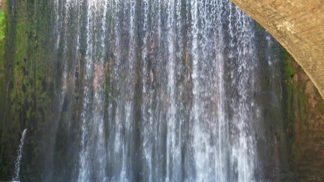 Paleokaria stone arched bridge and beautiful waterfall cascading into emerald green river pool on sunny day in Trikala region Greece. High quality footage
