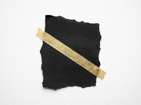 Realistic blank torn black paper fragment with gold metallic washi tape mockup on white background, isolated ripped edge card template for social media, scrapbook, or stationery design element.