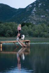 Fototapeta premium Woman Enjoying Peaceful Evening on Wooden Pier over Calm Lake with Mountain Reflections