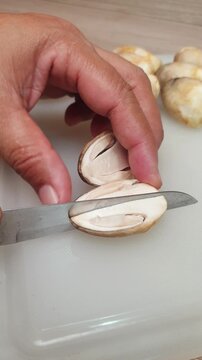 A person using a kitchen knife to slice fresh straw mushrooms on a white cutting board for meal preparation