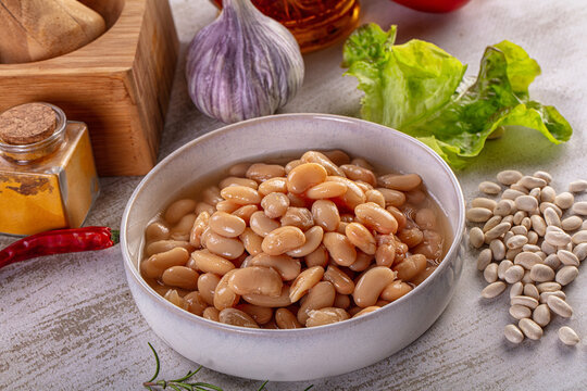 Bowl of cooked white beans with garlic chili and herbs on rustic table