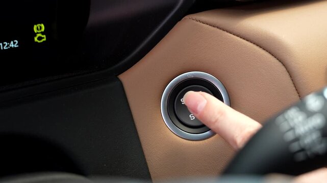 Close-up of a woman&rsquo;s index finger pressing the engine start button inside a modern car. Simple action showing vehicle ignition, automotive technology, transportation and everyday driving routin