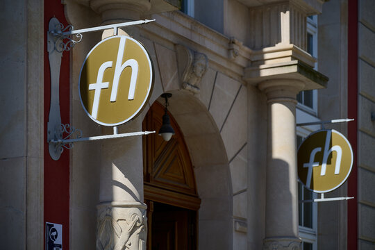 Round golden hotel or business signs with lowercase fh letters hanging on a historic stone building facade with columns, Gdansk, Pomeranian Voivodeship, Poland, Europe.
