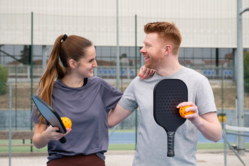Fototapeta premium Happy couple standing on a court, holding paddles and a ball, ready to play