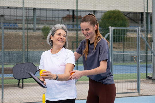 Two women smiling, having fun playing pickleball on a court