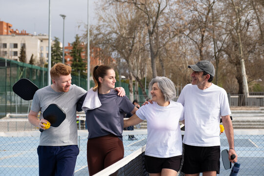 Group of diverse generations walking with arms around shoulders, holding pickleball paddles and ball
