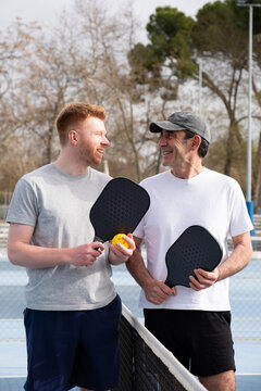 Two men enjoying a moment together on a pickleball court with paddles and ball