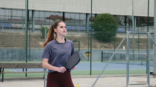 Athletic young woman playing pickleball and serving the ball during a match on an outdoor court
