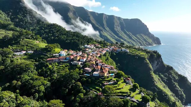 Aerial drone footage of a picturesque coastal village nestled on a lush green mountainside overlooking the sparkling blue ocean, cinematic travel destination