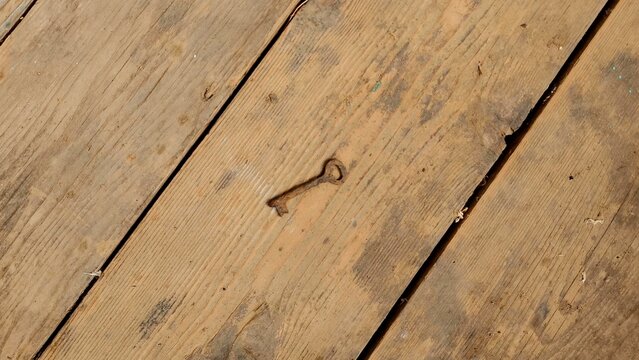 Close-up shot of a very old and rusty iron fireplace tongs tool lying on a rustic, weathered antique wooden floor texture.