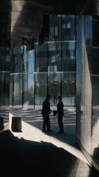 Vertical video of diverse young adult businessmen meeting and shaking hands outside modern office building. Footage is suitable for corporate partnership and B2B marketing campaigns