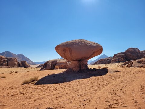 Famous mushroom rock formation standing alone in the vast orange sand desert of Wadi Rum, Jordan.