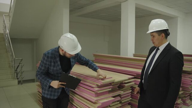 Two foremen in hard hats discussing building materials at a construction site