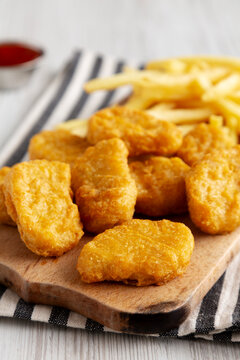 Unhealthy Chicken Nuggets and French Fries on a Wooden Board, side view.