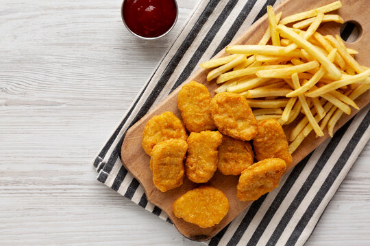 Unhealthy Chicken Nuggets and French Fries on a Wooden Board, top view. Copy space.