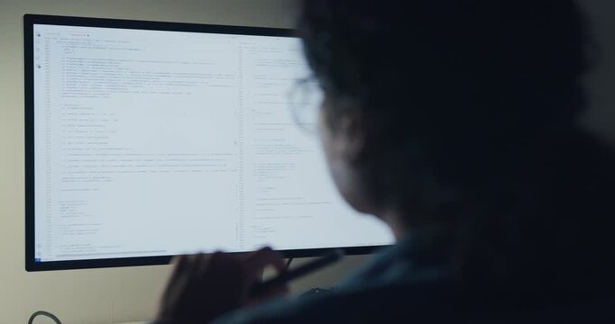 Close-up young Black female programmer coding AI software on multiple screens in night office. Network security, cybersecurity, machine learning, working late, overtime, robotics automation concept.