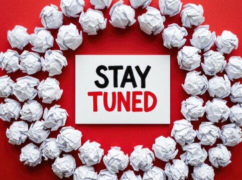 White paper sign with "STAY TUNED" text, surrounded by crumpled paper balls on red background, anticipation Concept and announcement, signifying a message of upcoming information or events.