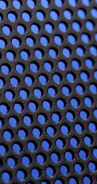 Black Perforated Metal Texture. Macro view of dark perforated surface with blue background visible through circular holes.