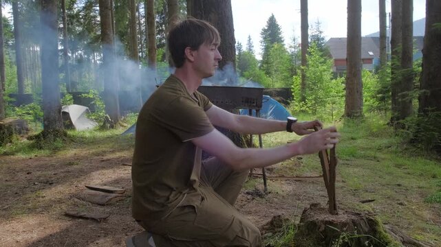 A horizontal tracking shot of a male camper using an axe to split wood logs for a campfire at a pine forest campsite, perfect for outdoor adventure branding and survival gear marketing.