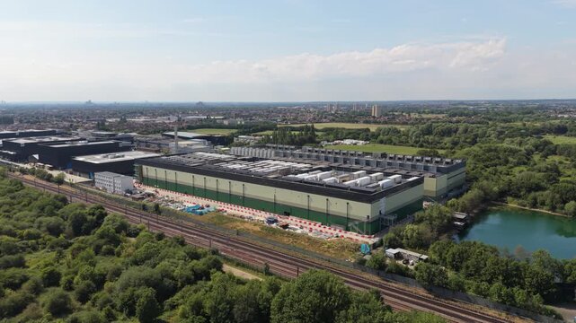 Expansive data center campus shown from above, featuring multiple buildings, a nearby natural lake, and active railway lines.