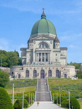 Low-angle vertical shot of Saint Joseph Oratory basilica with its green dome, long steps, and a clear blue sky.
