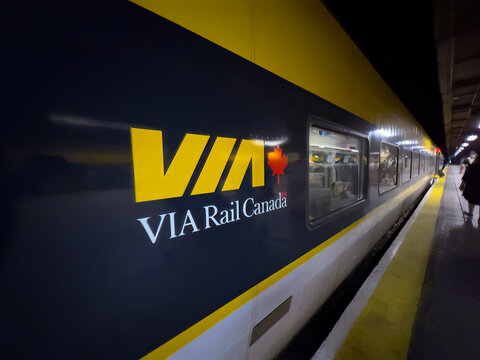 Montreal, Quebec, Canada. July 12, 2026. Angled close-up of a VIA Rail Canada passenger train car with its prominent yellow logo at night.