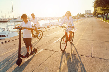 Obraz premium Family Riding Bikes and Scooter Along Marina Promenade at Sunset Parents and Son Enjoying Summer