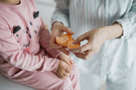 Mother peeling mandarin slices and giving them to her little child.