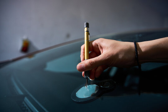 Technician uses a precision scriber to clean the glass damage point as an expert mechanic prepares the area for treatment during a professional windshield repair service