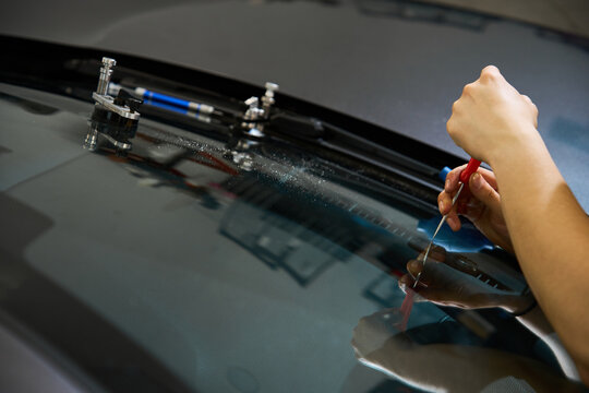 Windshield crack repair service. Expert mechanic uses specialized tool for final glass damage finishing. Final glass fracture inspection using scriber