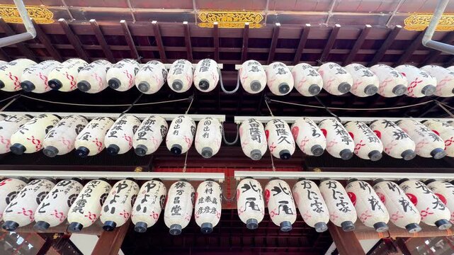 Rows of traditional Japanese lanterns with calligraphy hang under a shrine roof in Kyoto