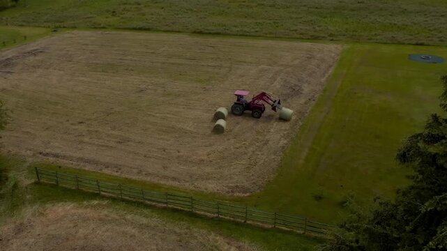 Modern tractor collecting and lifting freshly harvested hay bales on a working farm in the British countryside. Agricultural machinery handling forage during the harvest season, showcasing efficient f