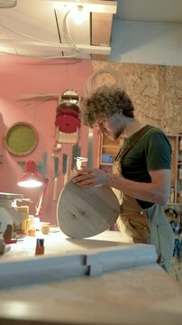 Carpenter manufacturing wooden furniture in workshop, using calipers to check precise fitting of chair details, wood workshop working progress, focused man examines stool parts before assembling.