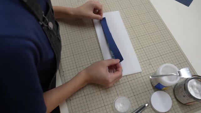 Craftsperson folds leather strip around cardboard template on cutting mat