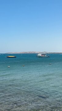 Beautiful coastal area near Red Sea hotels with sandy beaches, palm trees, sun loungers, warm clear turquoise water, very gentle waves, and sunny relaxing resort atmosphere.