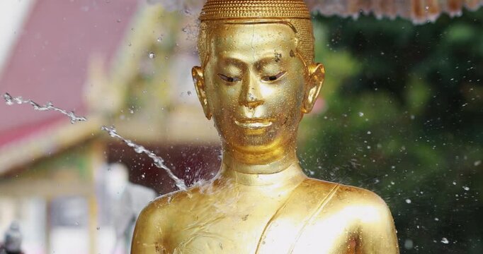 Golden Buddha statue with flowing water during the Songkran festival, Buddhist ritual, symbolizing faith, purity, peace, spirituality, meditation, and Asian cultural heritage in a serene atmosphere