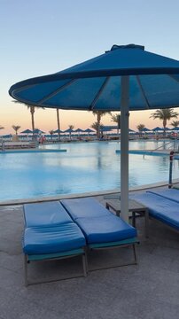 Evening loungers by the pool, calm water, soft lights, peaceful shadows, relaxation after sunset.