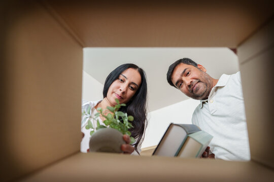 South Asian couple looking down into cardboard box while unpacking in new home