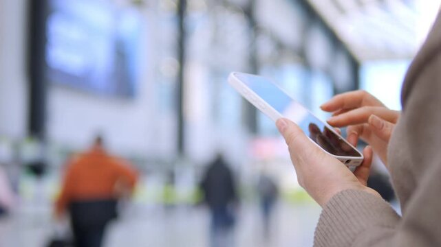 Person holds tablet in busy public space. Focused fingers tap screen, ignoring background movement. Ideal for tech, travel, or modern urban lifestyle themes