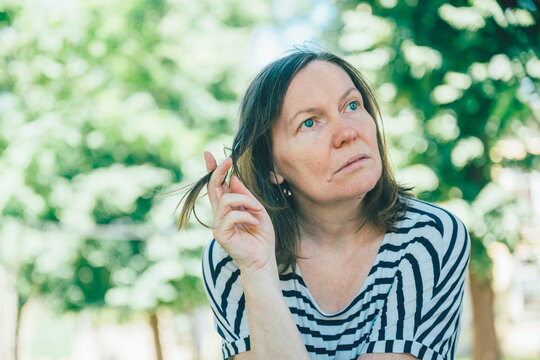 Pensive woman thinking outdoors portrait sitting in park on sunny day reflective mood,