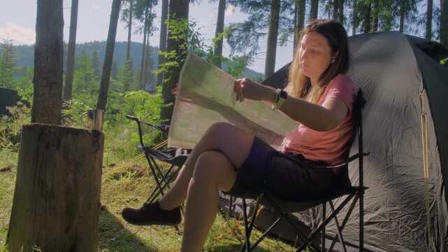 Female camper analyzing route on topographic paper map at forest camp
