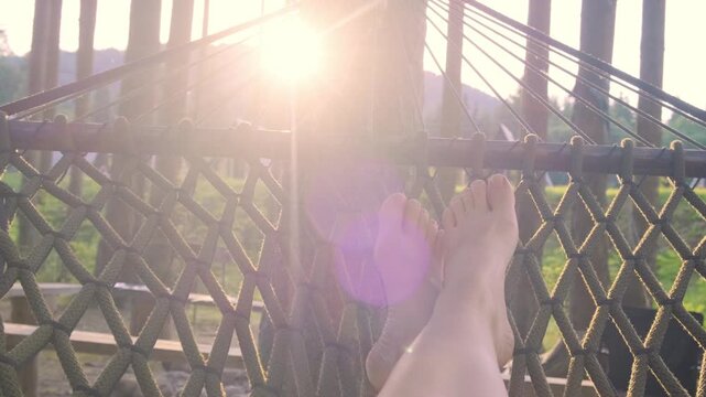 A horizontal close up shot from the perspective of a person resting their bare feet in a woven net hammock at a sunny forest campsite, ideal for wellness branding and vacation leisure advertising.