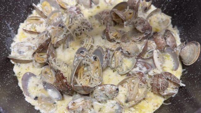 Cooking vongole clams in a wine-cream sauce on a skillet, garlic, parsley, steaming, rich seafood.