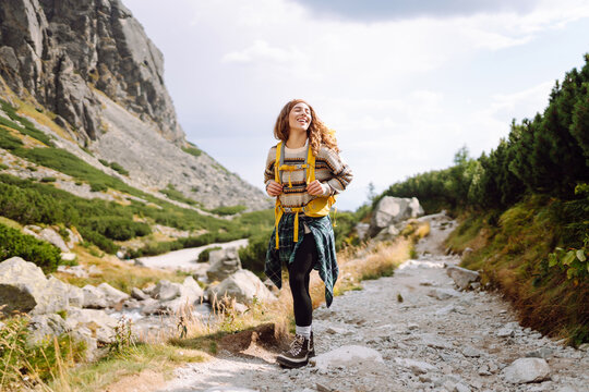 Young woman with hiking backpack walks along a rocky path surrounded by trees. A female hiker enjoys the mountain scenery at sunset. Concepts of relaxation, adventure, and activity.