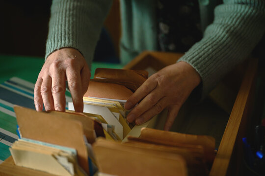 Close-up of female hands browsing old card catalog in rustic wooden crate, vintage research and archival concept
