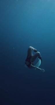Woman freediver gracefully swims underwater with fins in blue deep ocean, vertical screen